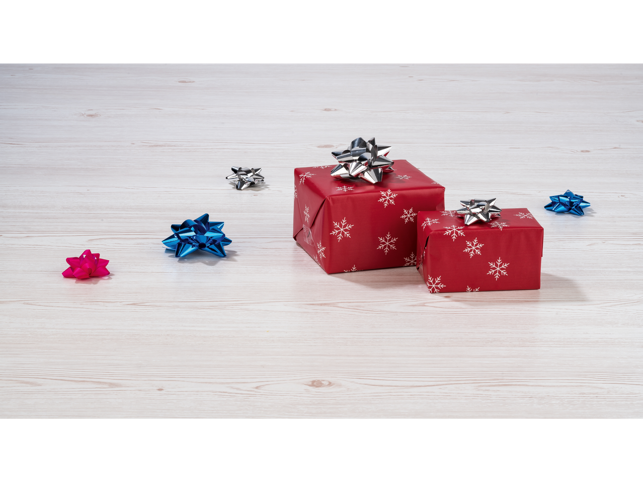 Црвени божићни поклони са сребрним машнама и разнобојним украсним машнама на дрвеној позадини.