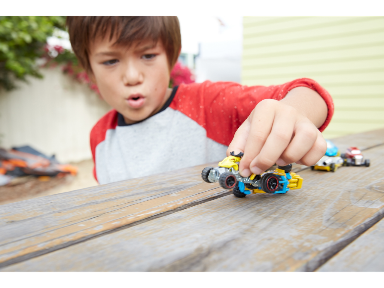 A child plays with Hot Wheels cars on a wooden table.