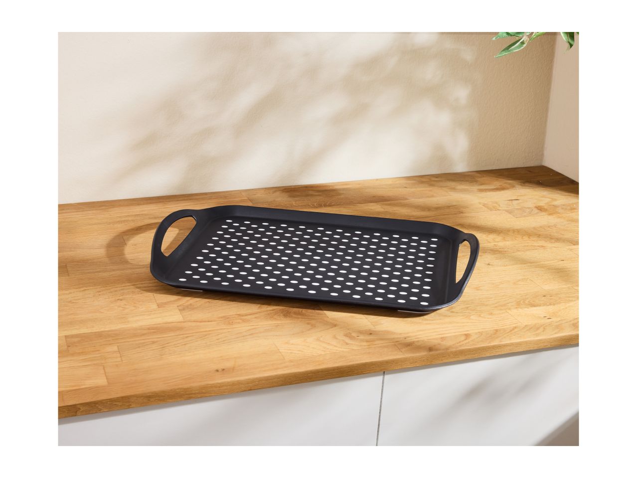 Black rectangular serving tray with perforated white dots on a wooden countertop.