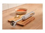 Immersion blender on a wooden cutting board next to a bowl of tomato soup, garlic, and thyme.