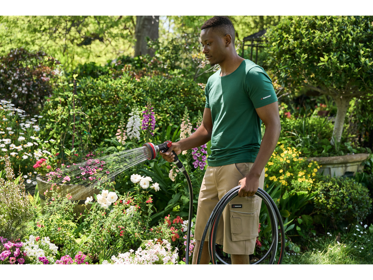 Man watering garden with Parkside Performance Multifunction Spray Gun and garden hose.