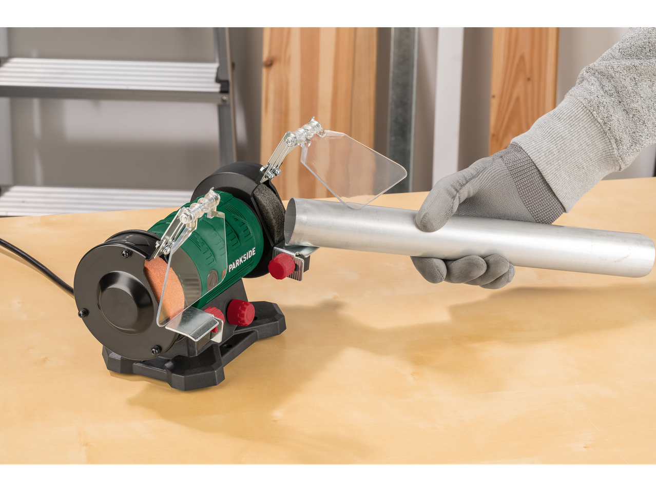 Un muncitor cu mănuși șlefuiește o țeavă de aluminiu pe o mașină de șlefuit Parkside.