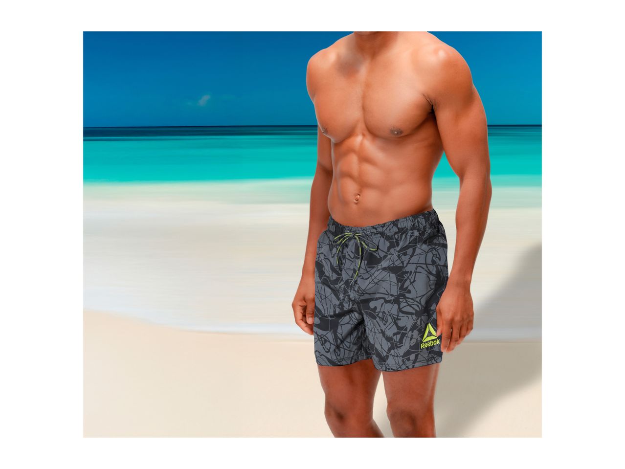 Man in grey patterned swim shorts with a neon green logo on a beach
