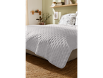 A light gray quilted bedspread sits neatly on a bed with a jute rug underneath.