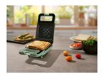 A light green sandwich maker with a grilled cheese sandwich inside, on a kitchen counter.