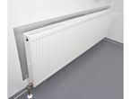 White radiator with a reflective foil behind it, on a white wall and gray floor.