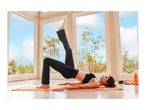Woman in black activewear doing yoga on an orange mat by a window.
