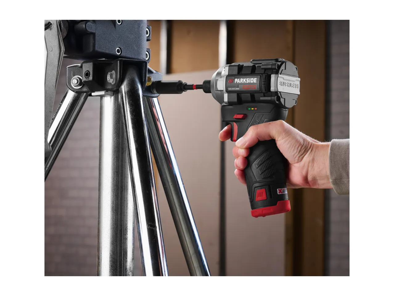 A person using a cordless impact driver to fasten something on a metal stand.