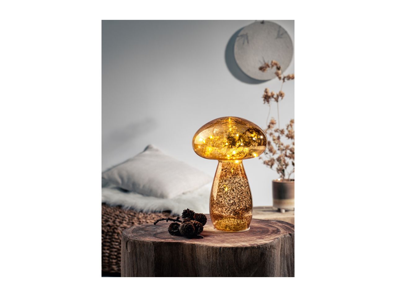 A mushroom-shaped lamp with warm lights on a wooden table with pinecones.