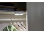 Uma pequena luz LED ilumina um armário com roupas penduradas.