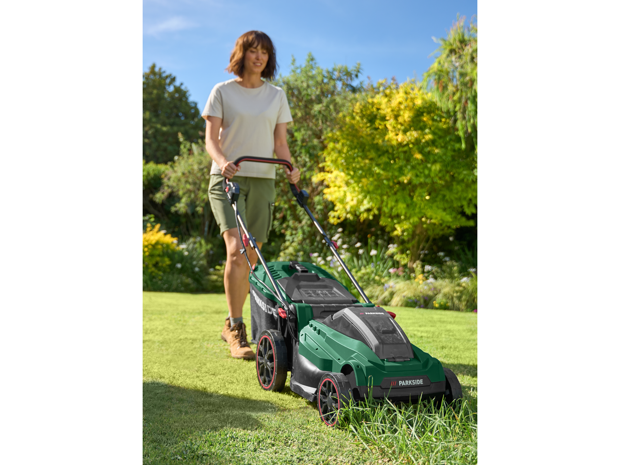 Woman mowing lawn with a green PARKSIDE® 40V Cordless Lawn Mower.
