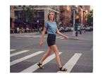 Woman in a blue t-shirt and black shorts walking across a crosswalk in the city.