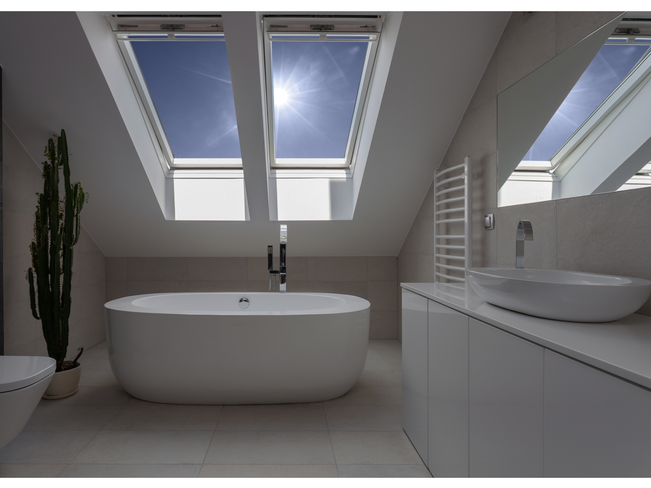 Baie modernă cu cadă, chiuvetă și ferestre de mansardă cu soare puternic.