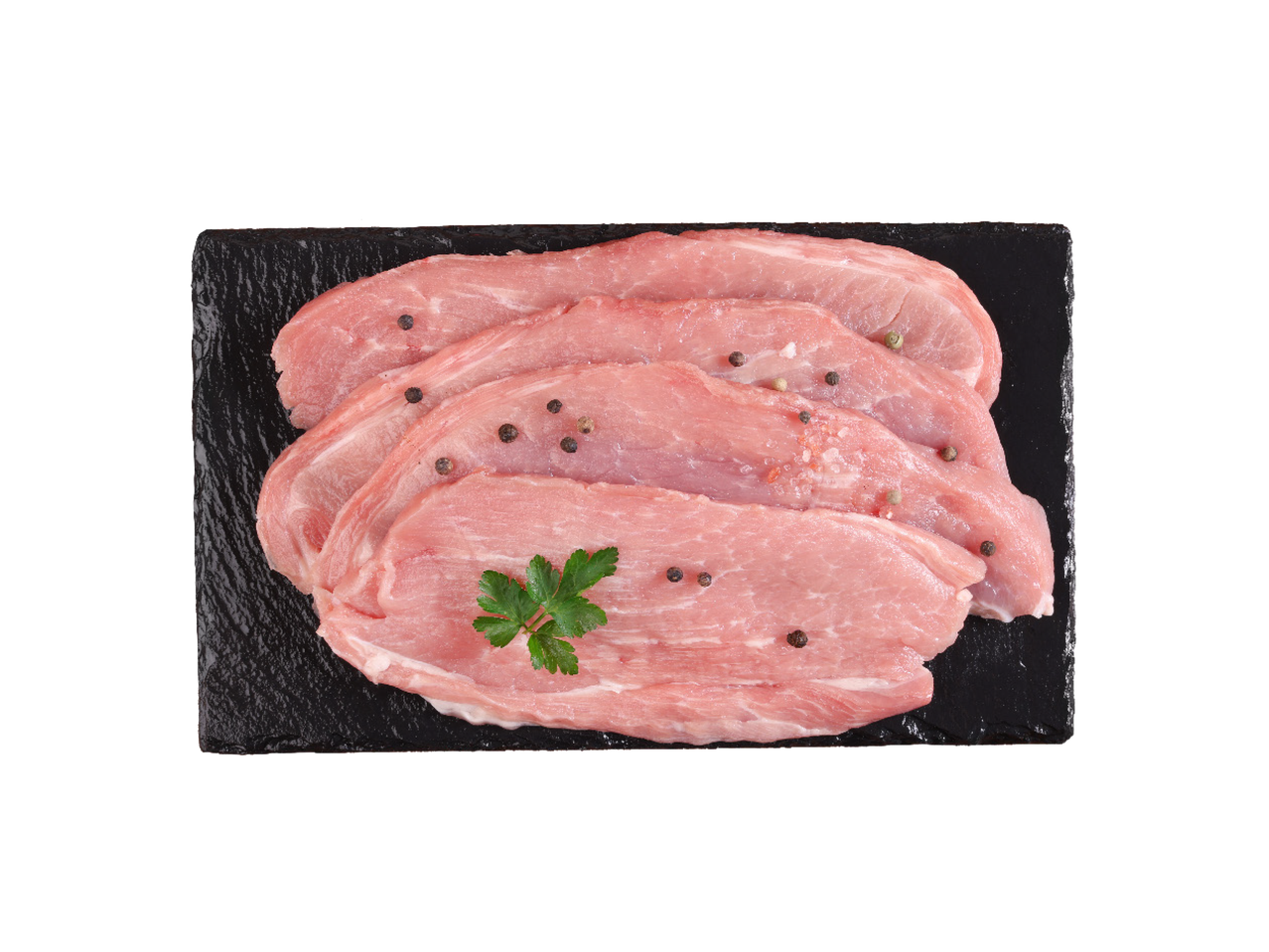 Sveži svinjski odresci sa biberom i peršunom na crnoj ploči.