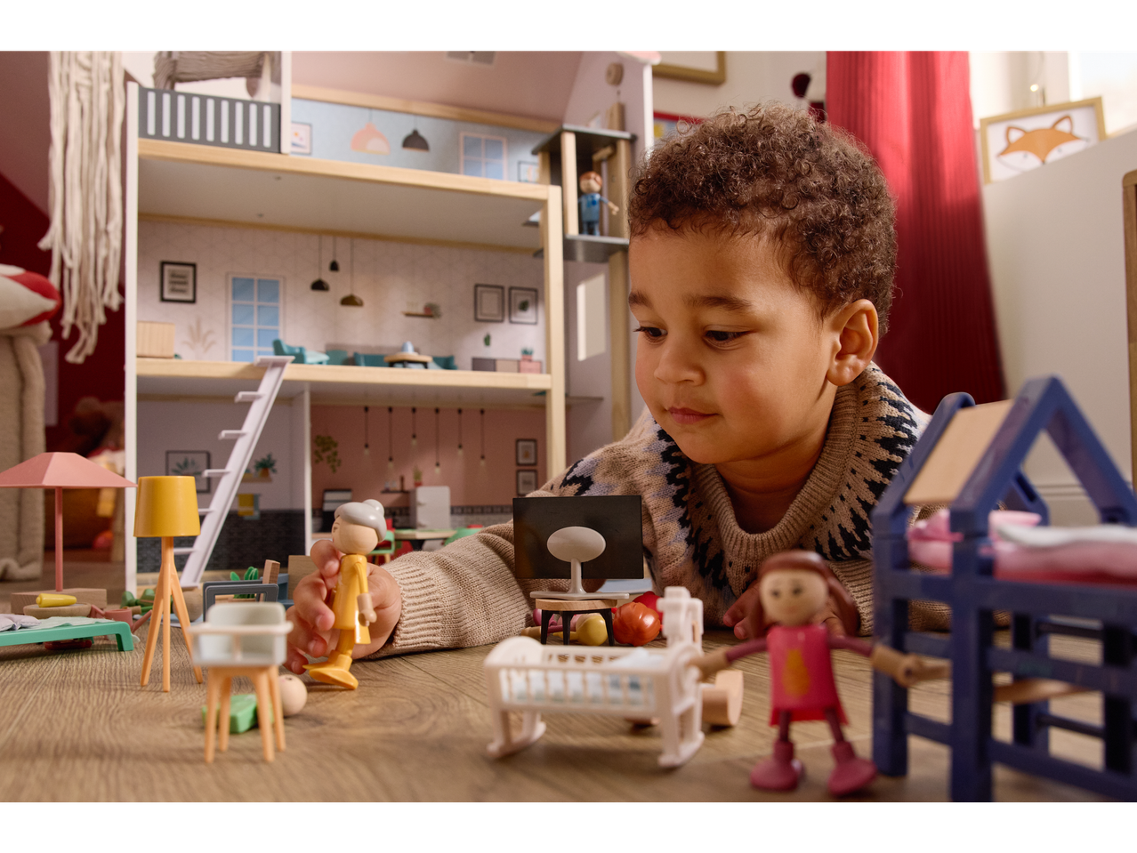 A child plays with a Lupilu wooden doll's house and various doll figures and furniture.
