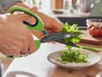 Mani che usano delle forbici per erbe aromatiche verdi per tagliare delle erbe aromatiche.