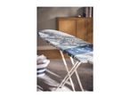 Ironing board with a blue and white patterned cover in a room with a wooden cabinet.
