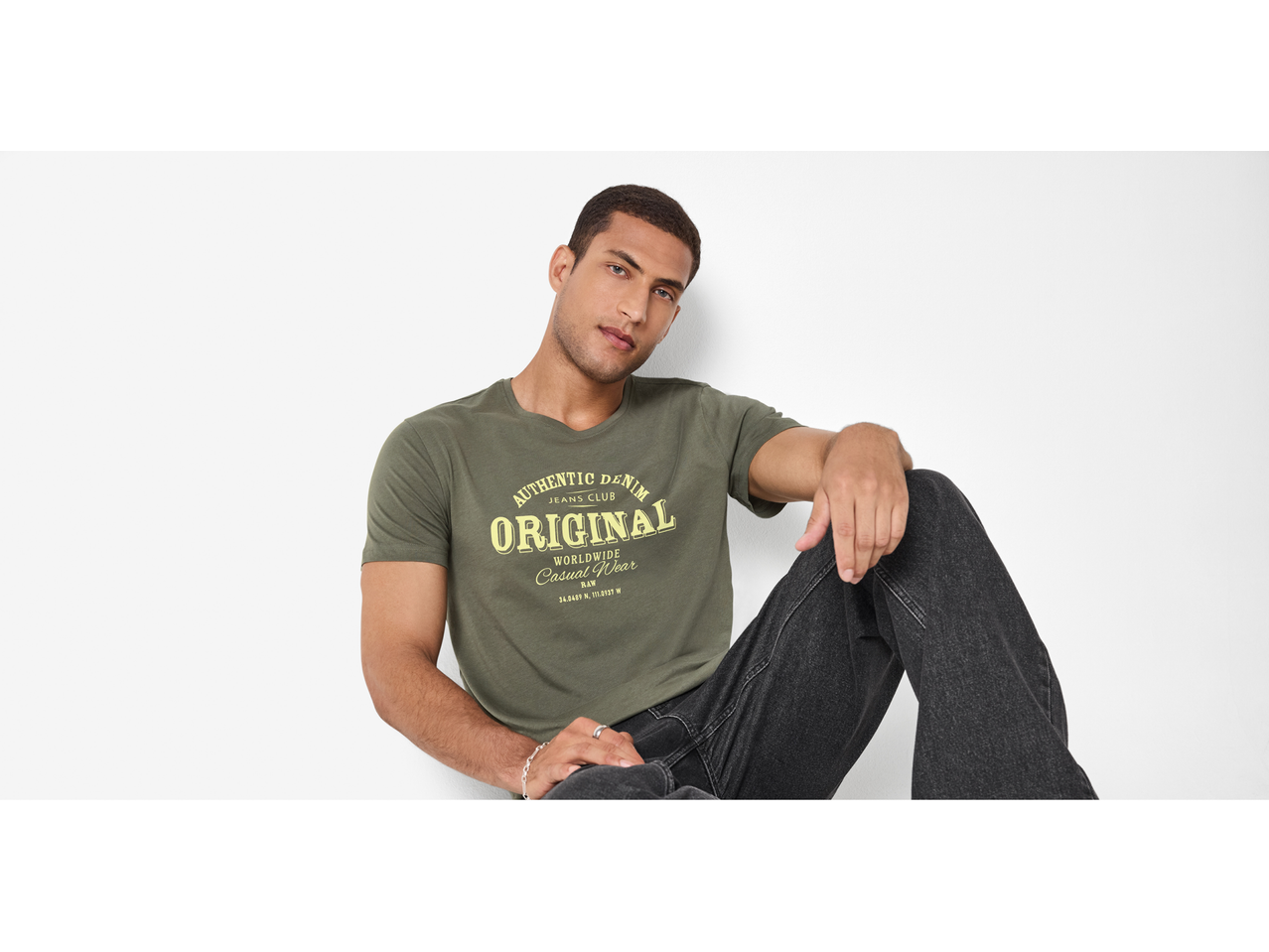 Muškarac u maslinastozelenoj majici s natpisom „AUTHENTIC DENIM ORIGINAL“ i crnim trapericama.