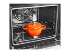 An orange cast iron pot with a lid inside a clean, empty oven on a metal rack.