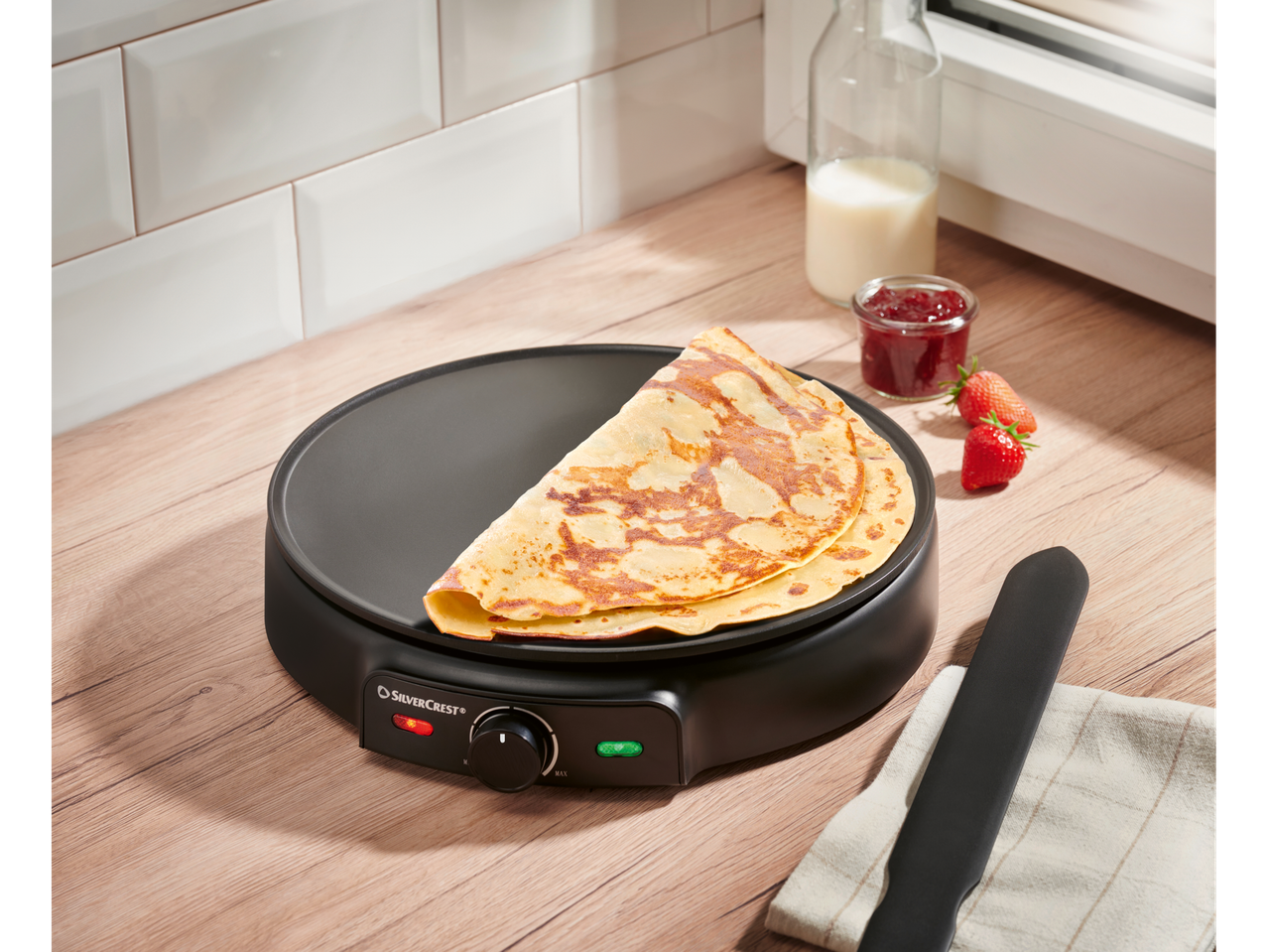 SILVERCREST® aparat za palačinke sa palačinkama, džemom i jagodama na drvenoj radnoj ploči.