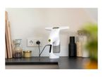 Window vacuum cleaner charging on a kitchen counter with various jars and cutting boards.