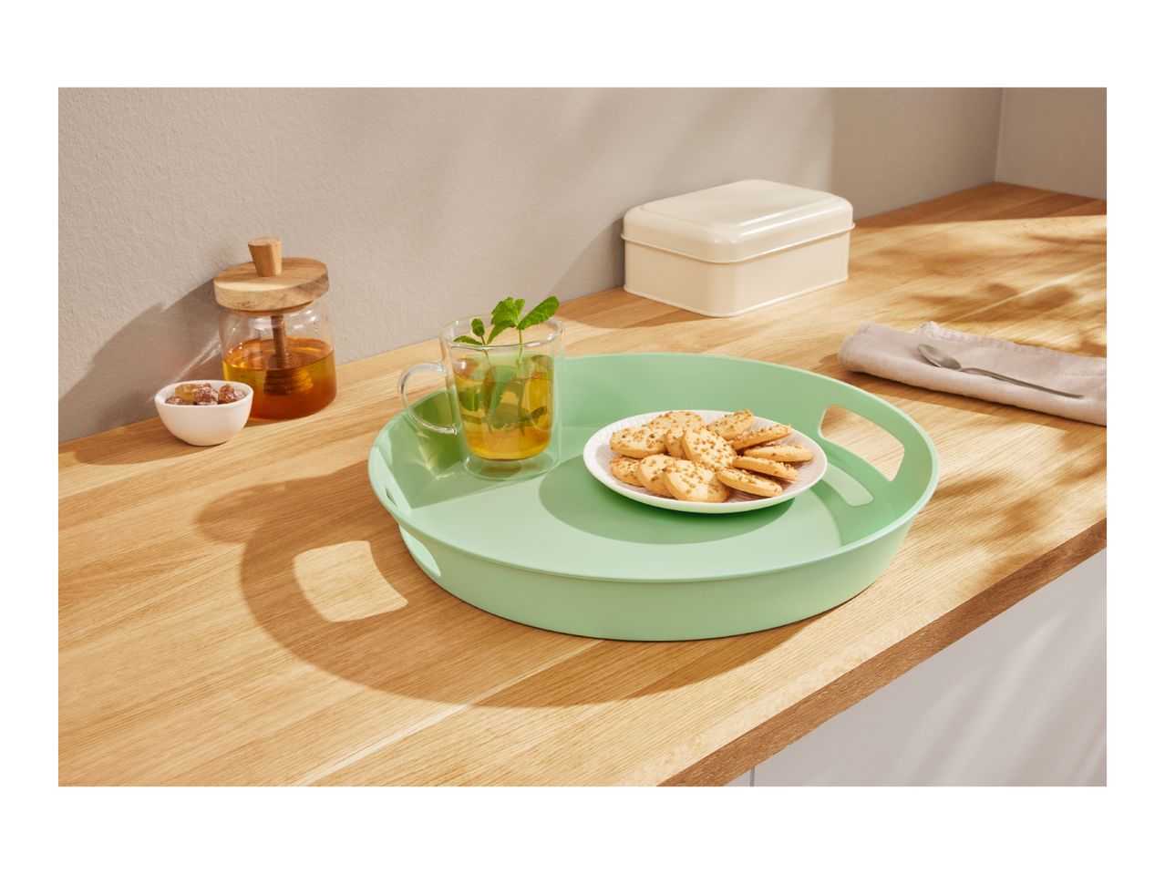 A light green serving tray with mint tea and cookies on a wooden countertop.