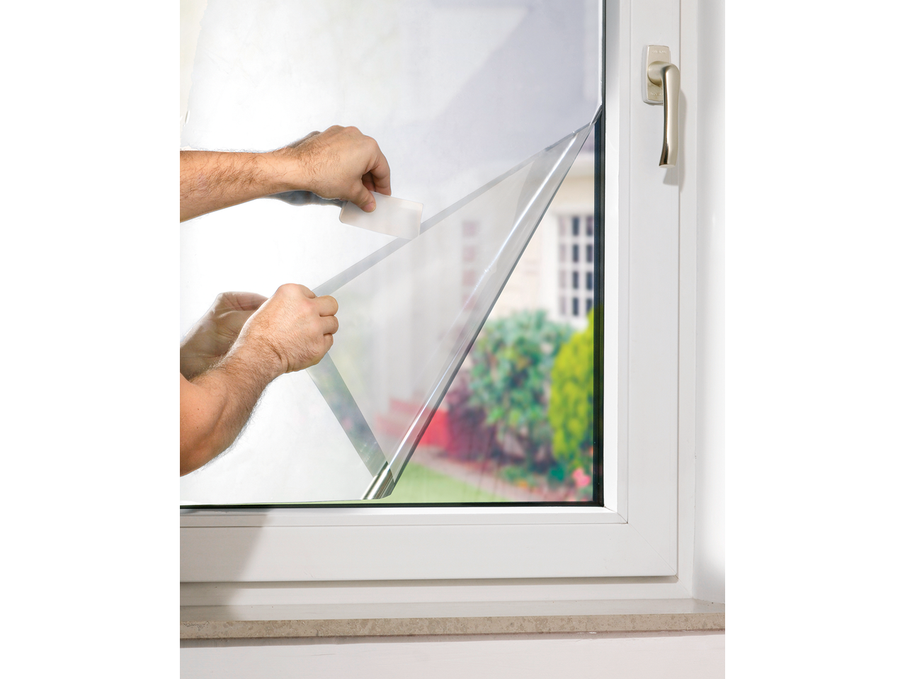 Bărbat aplicând folie de fereastră PARKSIDE cu o spatulă pe un geam.