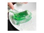 Hand squeezing green dish soap onto a green sponge in a white bowl with suds.