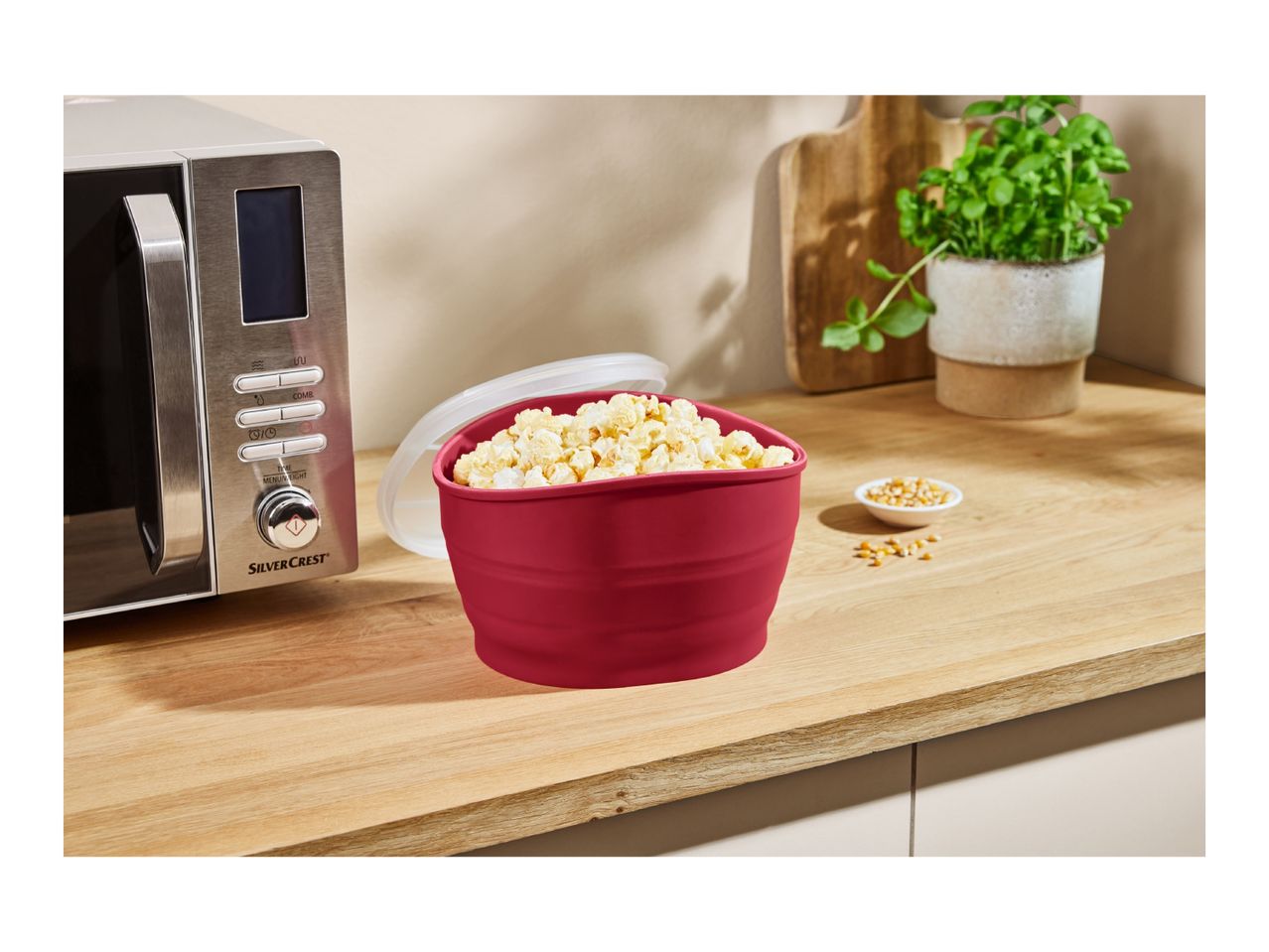 A SilverCrest microwave next to a red bowl of popcorn on a wooden counter.
