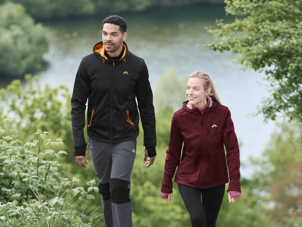 Zwei Personen in Outdoor-Jacken und -Hosen gehen einen Weg entlang.