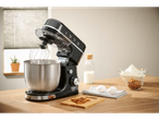 A black stand mixer on a wooden counter with baking ingredients.