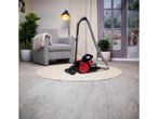 A red and black upright vacuum cleaner sits on a rug in a living room.