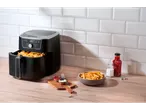 Friteuză cu aer cu cartofi prăjiți, ketchup și maioneză pe un blat de lemn.