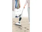 A person vacuuming muddy footprints on a wooden floor with a Bosch vacuum cleaner.
