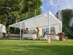 Family enjoying a meal under a white party tent in a garden with green grass.