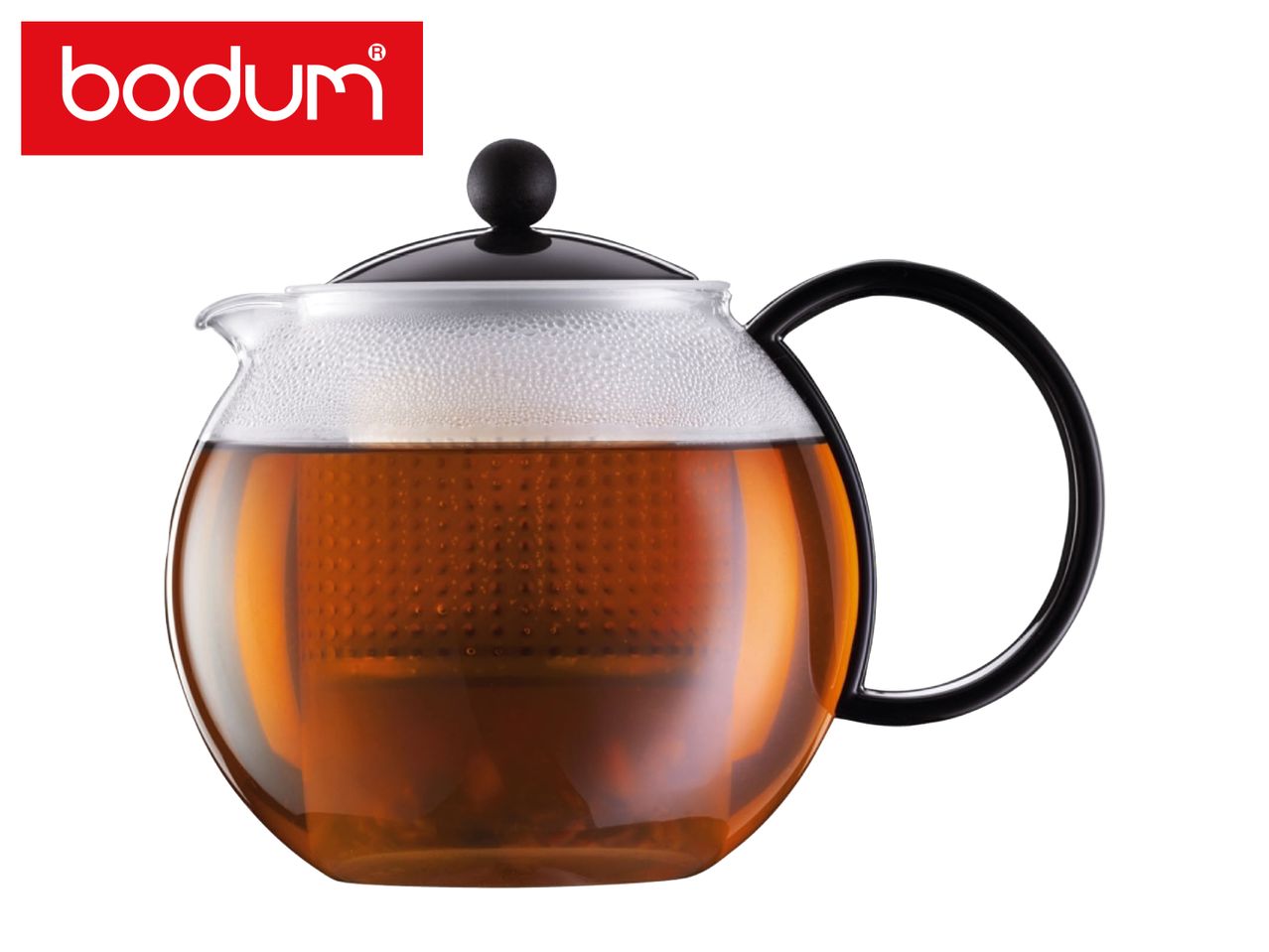 Glass teapot with black lid and handle, filled with amber tea, on a white background.