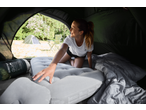 A woman inside a tent, reaching for an inflatable mattress, with a sleeping bag nearby.