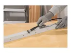 Hands in gloves using a rotary tool with a cutting disc on a white metal profile.