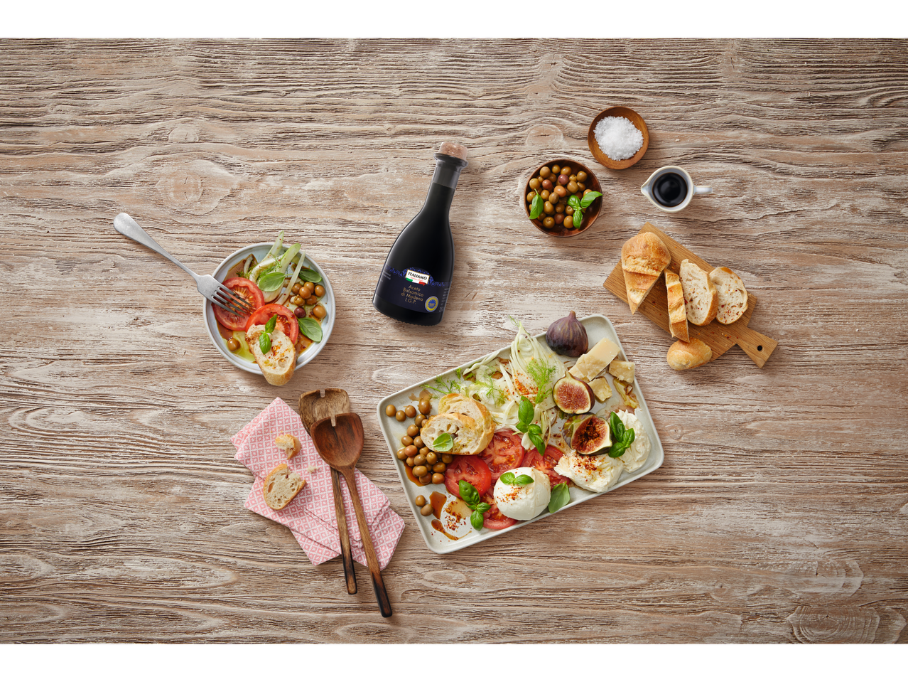 Een fles balsamicoazijn van Italiamo omringd door een salade, brood en een kaasplank.