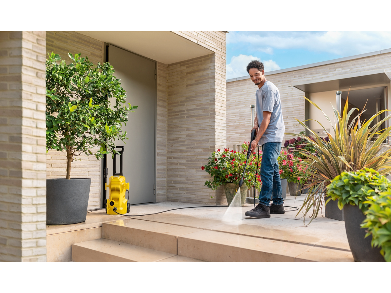 Bărbat curăță o terasă cu un aparat de spălat cu presiune Kärcher galben.