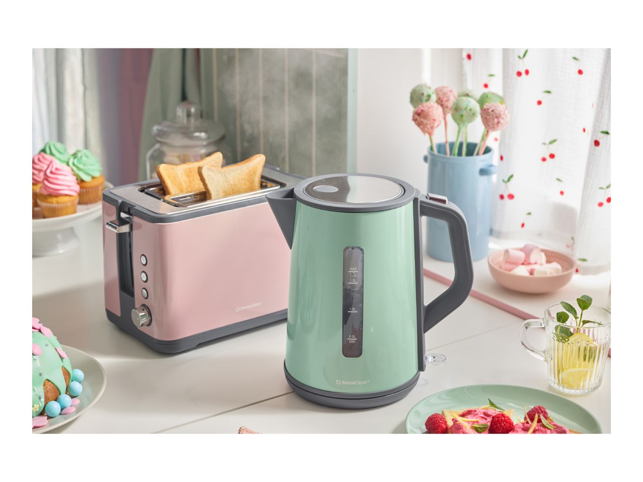 A pink toaster and a mint green kettle on a kitchen counter with various sweets.