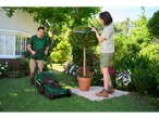 Homem a cortar relva com corta-relvas Parkside®, mulher a podar arbustos com tesoura de podar Parkside®.