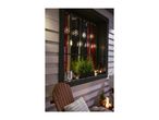 Outdoor window decorated with snowflake lights, small evergreen trees, and lanterns.