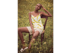 Model in summer dress and shorts sits on a chair in a field.