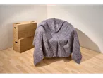Un scaun acoperit cu o pătură gri de mutare și două cutii de carton pe o podea de lemn.