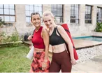 Două femei zâmbitoare, îmbrăcate în echipament sportiv, poartă saltele de yoga.