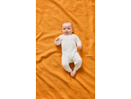 Lupilu® baby in a white sleepsuit with stars, lying on an orange waffle-knit blanket.
