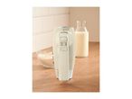 Cream-colored hand mixer standing upright on a wooden countertop next to baking ingredients.