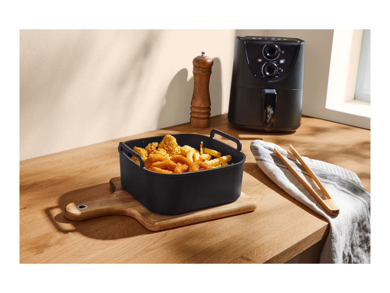 Air fryer with a basket of fried food (fries, onion rings, chicken nuggets) on a wooden board.