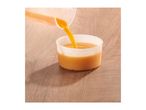 Orange juice being poured from a measuring jug into a plastic cup on a wooden surface.